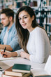 © BullRun - Long haired woman writing at table in library and looking at camera