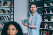 © BullRun - Serious multiracial women looking at laptop while smart man smiling with book at bookshelves
