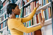 © BullRun - Focused ethnic student picking book from bookcase