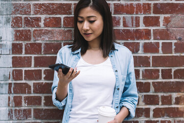 Wall Mural - Asian woman using smartphone and drinking coffee on street