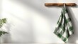 © JoxyAimages - A minimalistic kitchen towel with a green checkered pattern hanging from a rustic wooden hook against a plain wall evokes simplicity and elegance in design.