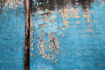 Poster - A close-up of a weathered blue wall with peeling paint and a rusty pipe. The texture is rough and aged, creating a vintage and rustic background. Cracked Rustic Blue Wall Texture Background.