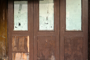 Poster - Close up of a weathered wooden door with faded glass panels. The door is made of brown wood, and the glass panels are covered in faded scratches. Old Wooden Doors with Faded Glass Panels.