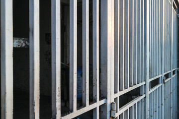 Poster - A gray metal gate made up of many thin bars seen from an angle.  Sun shining through the bars casts light and shadows.