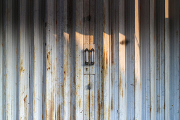 Poster - Closeup of a rusty metal door with sunlight shining through the slats, casting shadows. Rusty metal door with a handle with sunlight.