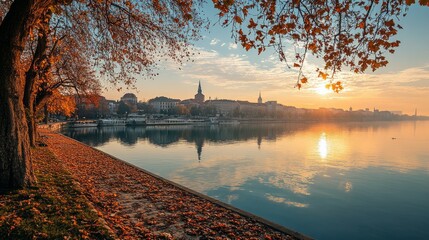 Wall Mural - A picturesque cityscape with a river reflecting a golden sunset, surrounded by autumn foliage.