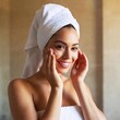© LIGHTFIELD STUDIOS - beautiful young woman with towel and head of head looking at camera while applying moisturizing cream in her bathroom in the morning