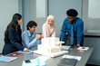 © Jestercine - Diverse team of professionals gathered around a table, discussing an architectural model and plans during a creative office meeting.