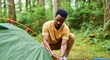 © Anna - Man setting up tent in forest campsite during summer day