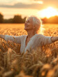 © sergign - An elderly lady joyously stands in a wheat field, arms raised, enjoying the golden sunlight around her.