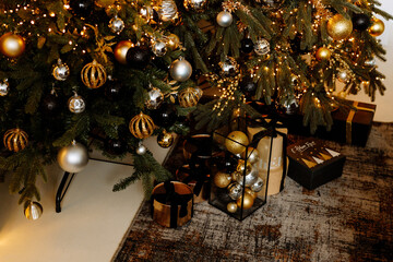 Black and gold gift boxes under the decorated Christmas tree at home.