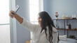 © Krakenimages.com - Young woman taking a selfie in a spa room while wearing a white robe, capturing the serene wellness environment with shelves of beauty products in the background
