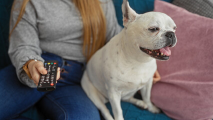 Wall Mural - A young woman sits in her living room with a remote in hand, accompanied by her happy canine pet.