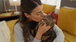 © Krakenimages.com - A young hispanic woman kisses her tabby cat while sitting on a bed in a cozy, colorful bedroom at home.