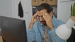 © Krakenimages.com - Hispanic man with moustache in office, focused on computer screen, holding head with both hands, appearing stressed in workplace environment.
