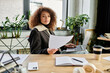 © Bliss - A determined woman is reading papers while seated at her desk, surrounded by plants and sunlight.