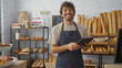 © Krakenimages.com - Young man smiling in a bakery shop with bread in the background while holding a tablet and wearing an apron