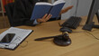 © Krakenimages.com - Female judge reading book in office with gavel, computer, and legal documents on desk
