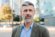 © Jose Calsina - Confident mature businessman looking at camera with a serious expression, professional man with beard in a suit jacket standing outdoors in an urban setting, exuding leadership and experience