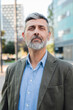 © Jose Calsina - Vertical. Confident mature businessman looking at camera with a serious expression, professional man with beard in a suit jacket standing outdoors, exuding leadership and experience