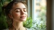 © BISO - Calm young woman with closed eyes and wind-swept hair, inhaling deeply by the window in her home.