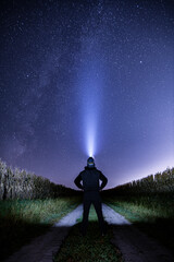 Wall Mural - Person standing on a dirt road/ dirt tire tracks surrounded by corn fields looking up at a star filled with a headlamp on in Iowa. 