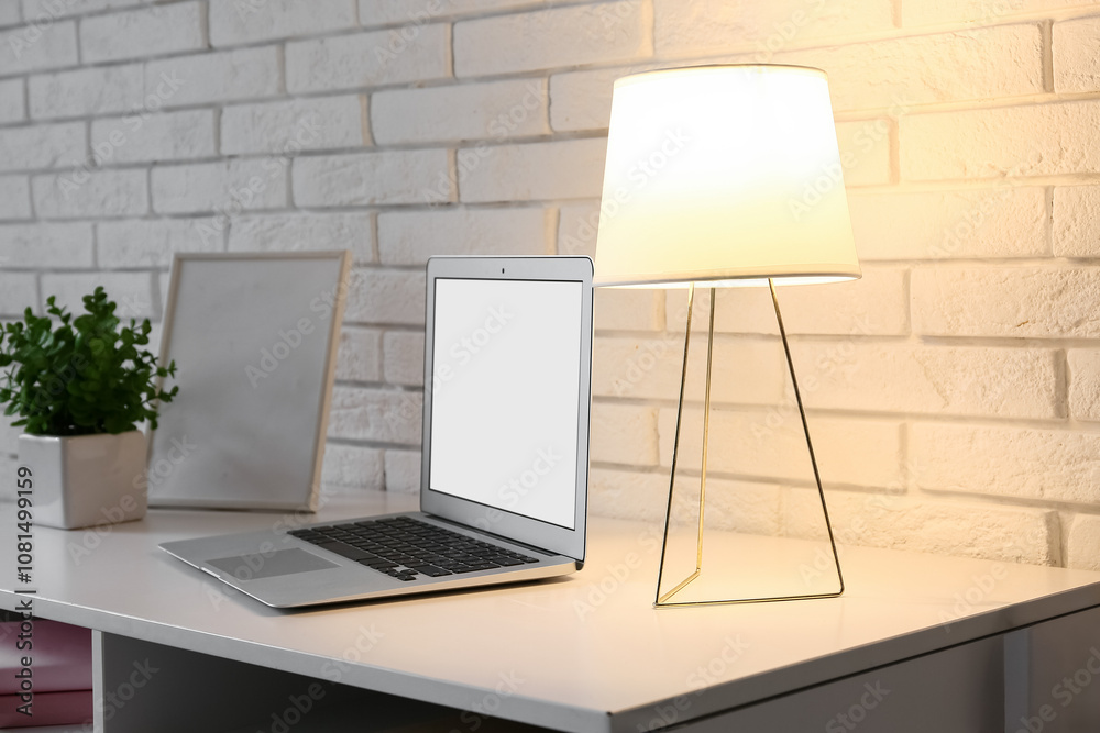 Comfortable workplace with modern laptop and glowing lamp on table, closeup
