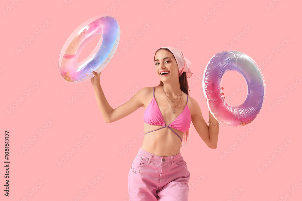Pretty young woman with inflatable rings on pink background
