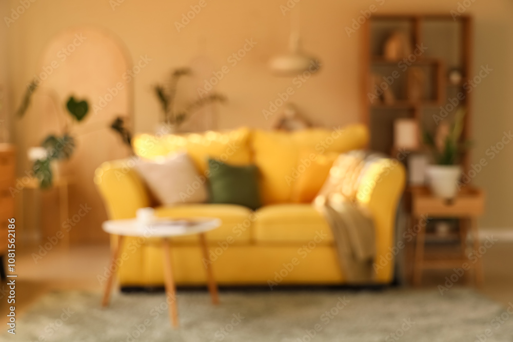 Interior of stylish room with comfortable yellow sofa and coffee table, blurred view