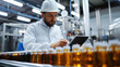 © Liana - Young factory worker in a white uniform checks production data in a bright factory setting