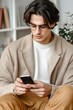 © Nataliya - A young man wearing glasses checks his phone while seated in a cozy, well-lit room lined with bookshelves and indoor plants