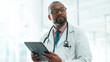 © peopleimages.com - Black man, doctor and tablet for thinking in hospital with medical research, Telehealth and surgery schedule. Male surgeon, healthcare and digital of history report, patient information and diagnosis