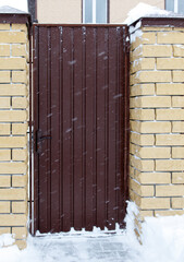 Wall Mural - A brown door with snow on it is in front of a brick wall