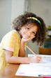© Cavan Images - Smiling child in yellow dress writing with a pencil at a table