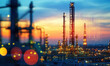 © Kim - Silhouetted industrial complex at sunset, illuminated by bright lights, evokes sense of power and industry
