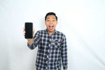 surprised and shocked asian man showing smartphone empty screen wearing casual plaid shirt isolated on white background