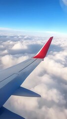Aufkleber - Airplane wing with red winglet soaring through a clear blue sky, fluffy white clouds spread out below, creating a breathtaking aerial view during a daytime flight