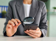 © Nadzeya - Businesswoman using smartphone with magnifying glass