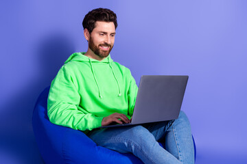 Photo portrait of pretty young male sit beanbag hold netbook wear trendy green outfit isolated on purple color background