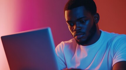 Poster - Focused Young Man Engaged with Laptop in Modern Setting Under Colorful Lighting Ideal for Technology and Lifestyle Themes