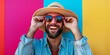 © StockUp - A joyful man wearing sunglasses and a hat poses happily in front of a vivid, colorful background outdoors.