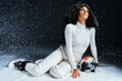 © LIGHTFIELD STUDIOS - A fashionable brunette woman in a ski suit poses gracefully in a snowy studio setting.