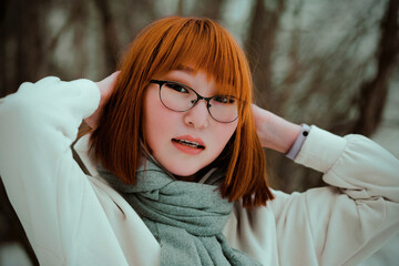  A portrait of a beautiful ginger Asian woman in a white hoodie and a scarf in a park on a winter day.