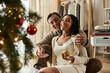 © LIGHTFIELD STUDIOS - A loving couple laughs and shares warmth by the Christmas tree in their holiday moment.