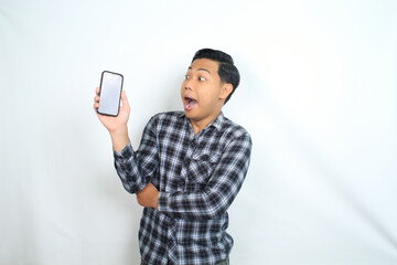 surprised and shocked asian man showing smartphone empty screen wearing casual plaid shirt isolated on white background