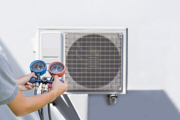 Air conditioning, HVAC service technician using gauges to check refrigerant and add refrigerant.	