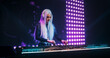 © Gorodenkoff - Portrait of a Beautiful DJ Making a Show on a Vibrant Stage, Entertaining a Large Audience in a Concert Hall. Music Producer Dancing on Stage and Using Turntables to Mix the Party Songs