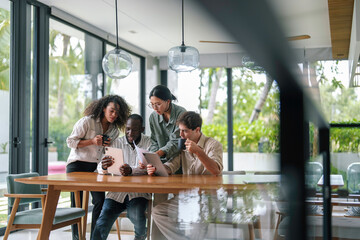 Wall Mural - A group of young adult professionals of diverse ethnicities work diligently in a sleek modern office, exchanging ideas over digital devices, reflecting teamwork and strategy.