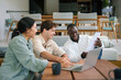 © Dorde - Three diverse young adults are deeply engaged in a work meeting in a cozy office lounge, utilizing a laptop and documents, dressed in casual professional attire.