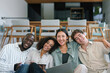 © Dorde - A group of young adult executives from diverse backgrounds sit closely in a contemporary office lounge, engaging with digital devices and sharing a joyful moment.